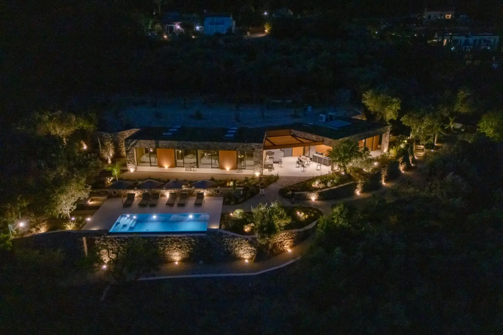 La villa e la piscina illuminate di notte tra le fasce di ulivi