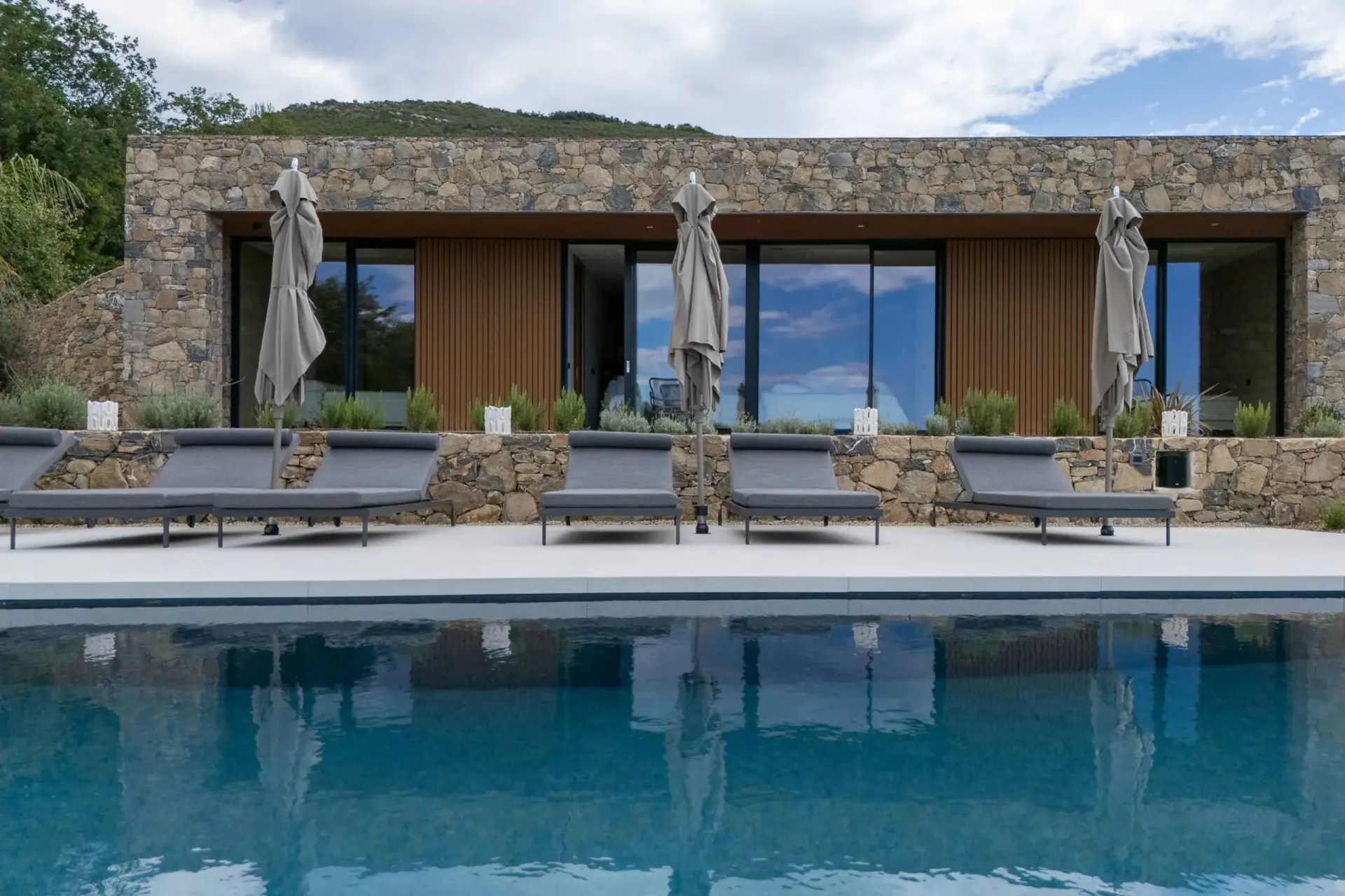 Facciata in pietra della villa riflessa nella piscina, con lettini e ombrelloni