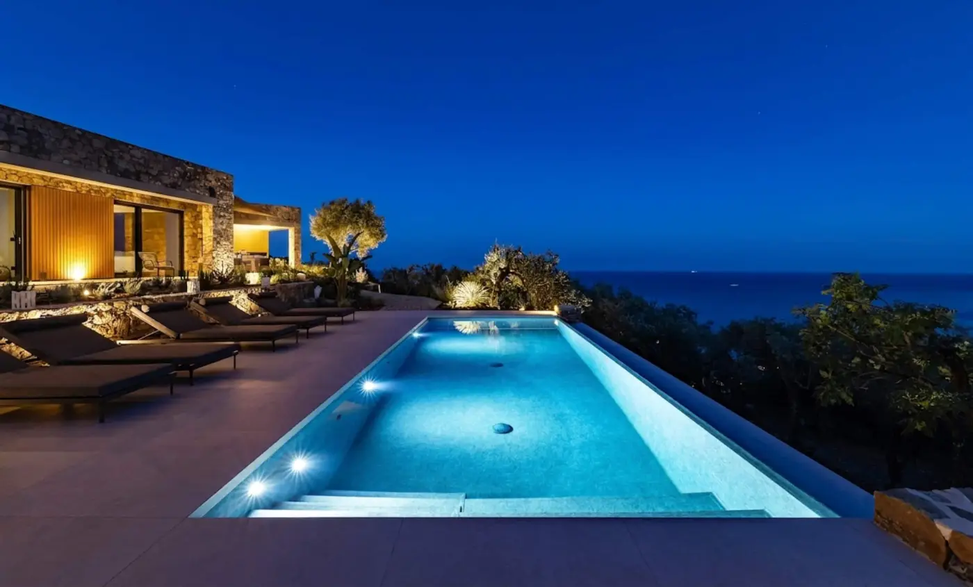 Piscina a sfioro illuminata al tramonto, con i lettini lungo la villa